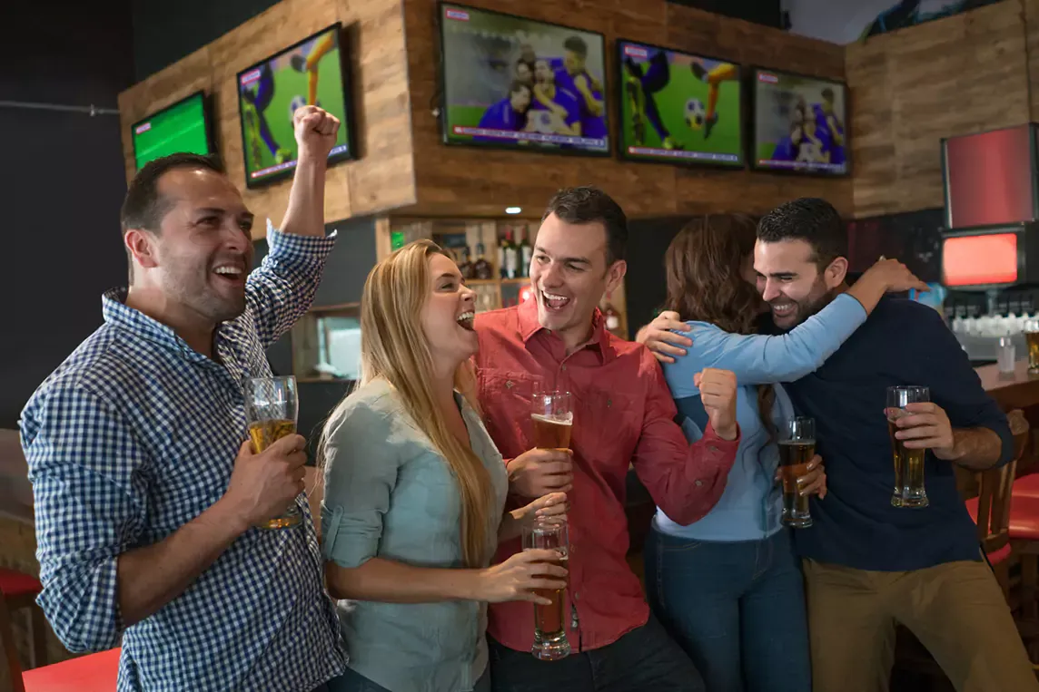 Excited friends celebrate while watching a soccer game on tv.