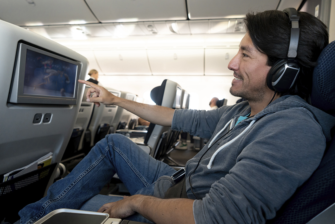 Man on an airplane watching movie on the seat back in front of him.