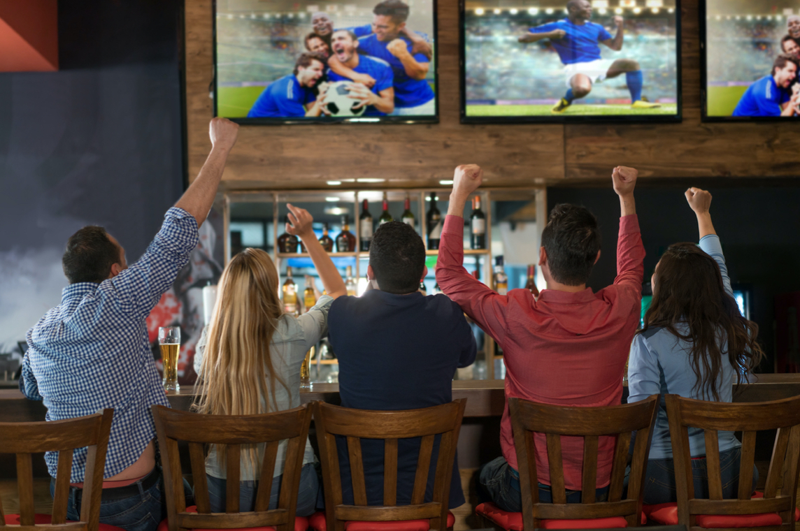 Customers cheer as they watch soccer on TV's at a bar.